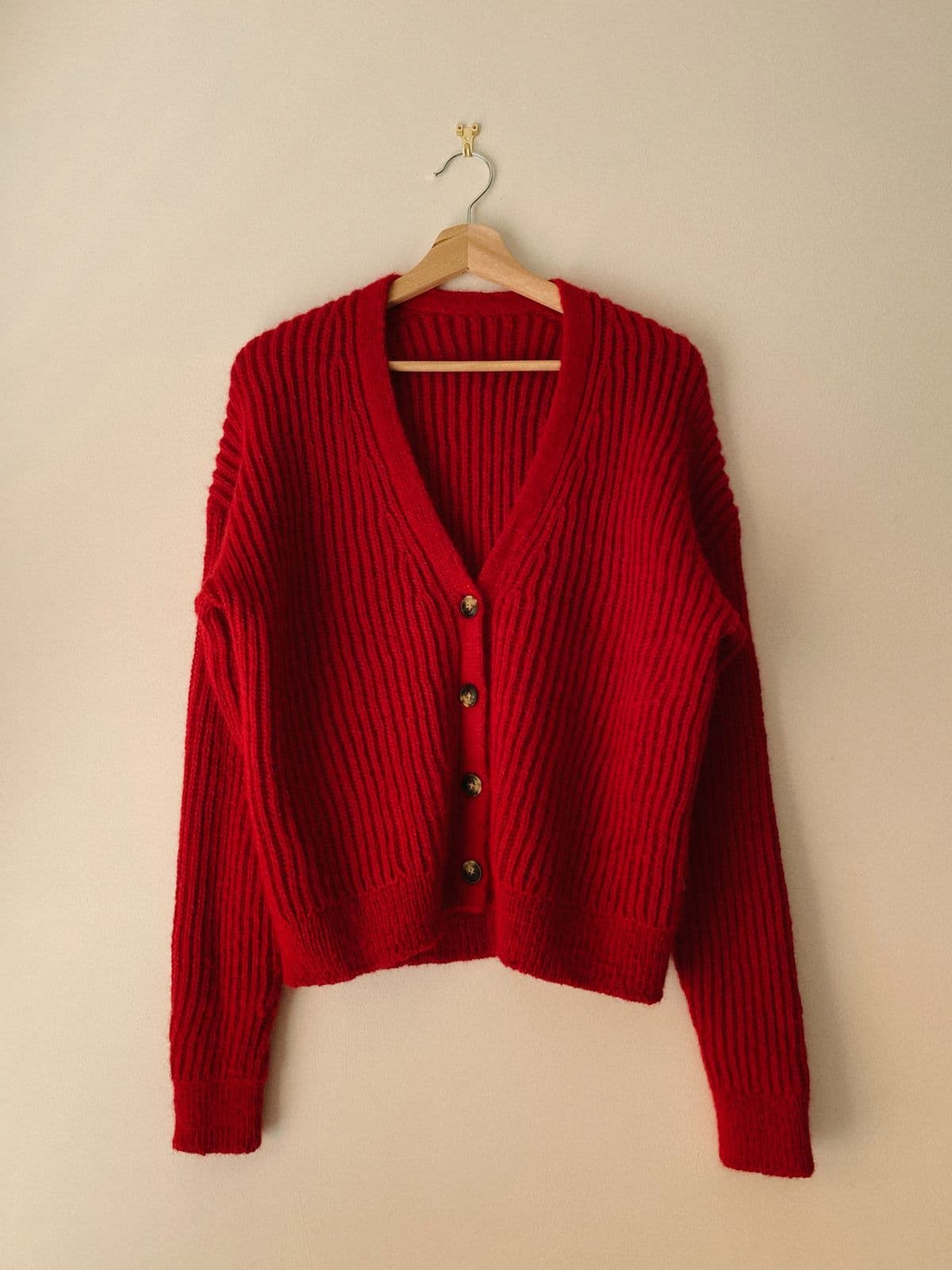 Red ribbed knit cardigan on a wooden hanger, from the illustrative product example