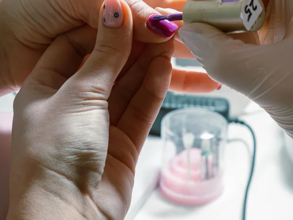 Nail artist applying berry colored polish during a manicure