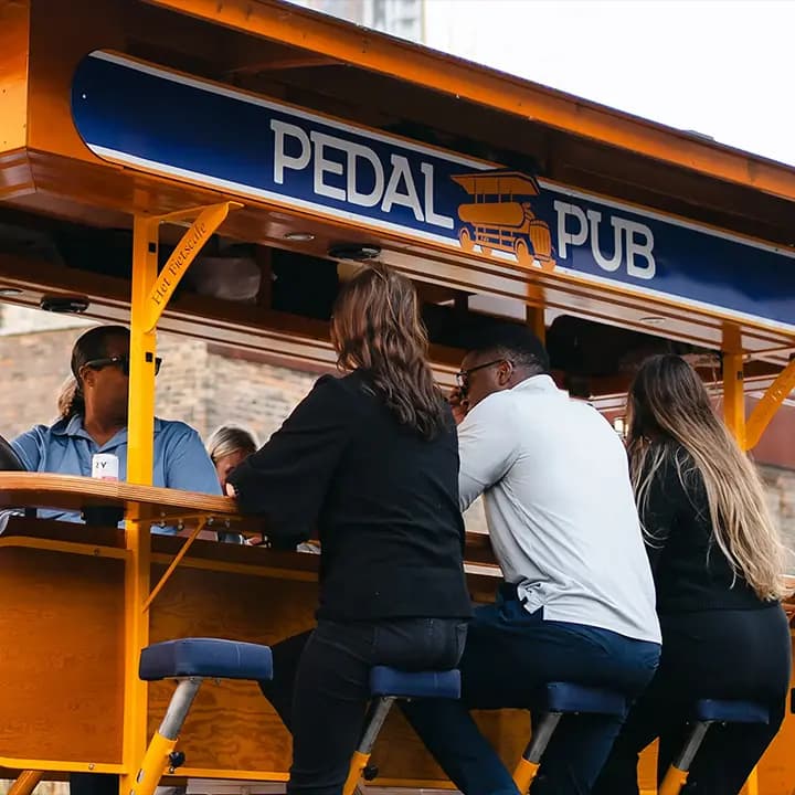A group of friends running toward a Pedal Pub bike, some wearing party hats