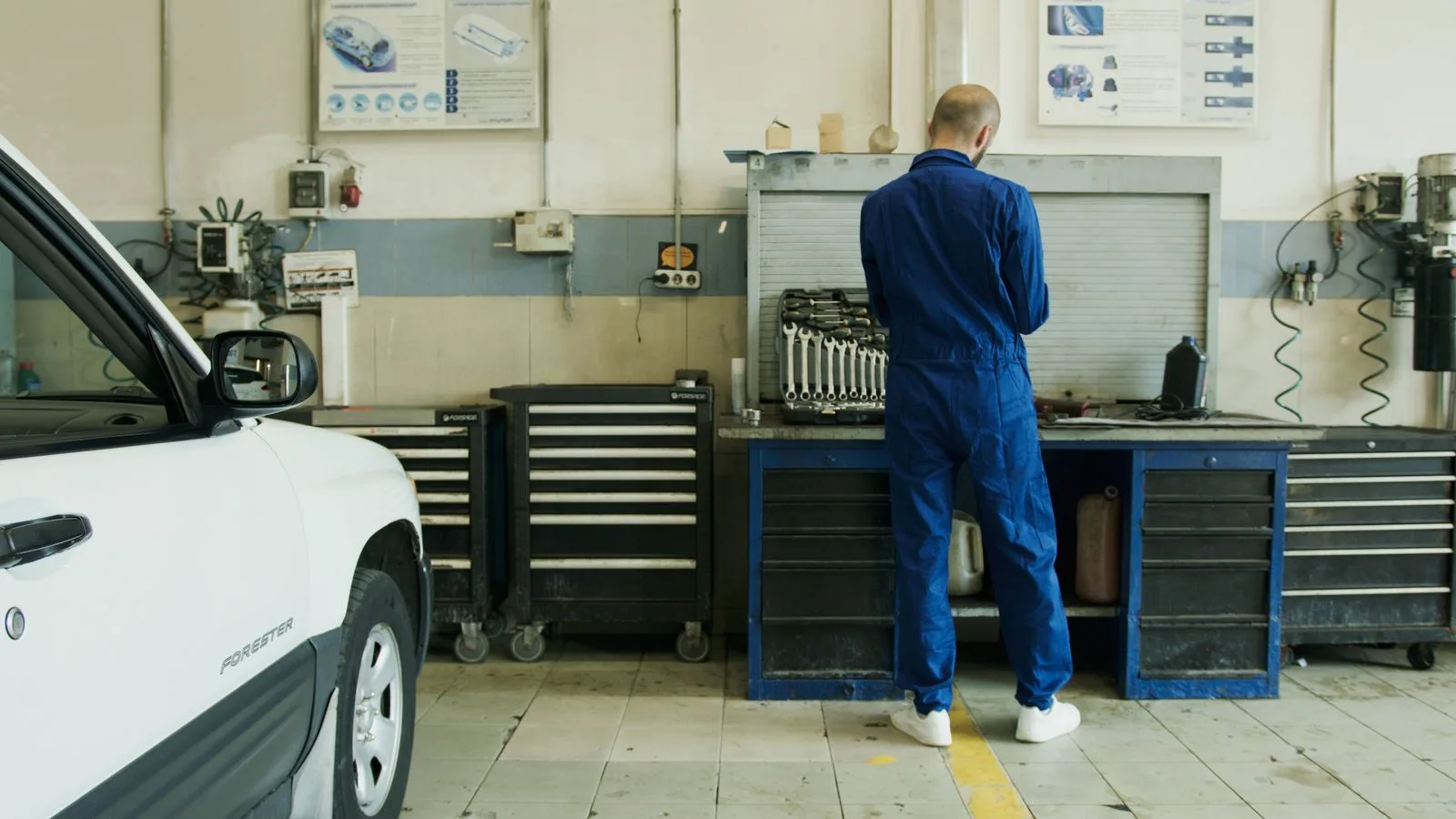 A mechanic in blue overalls inspecting a white car in a service garage