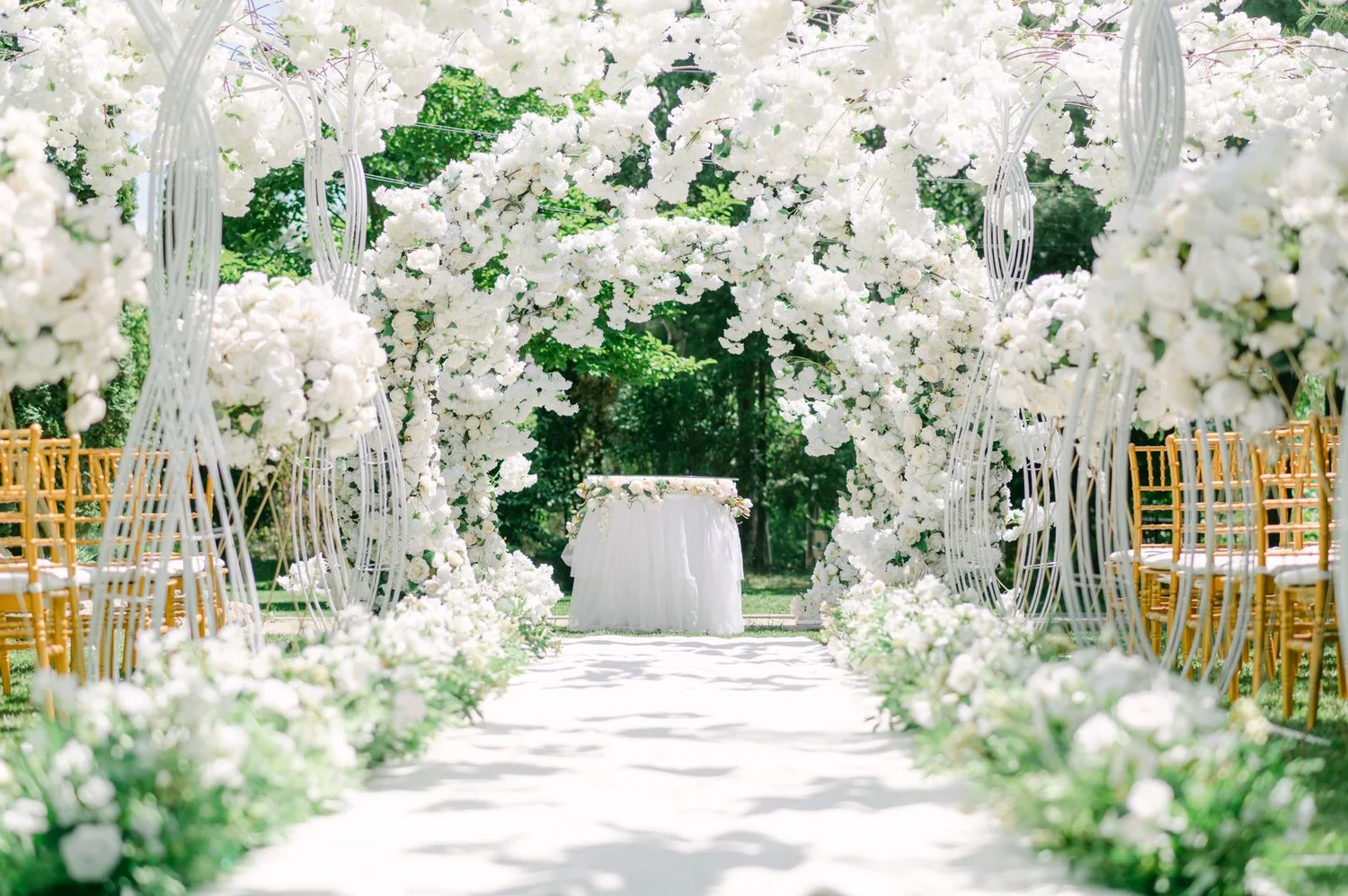 A sunlit garden ceremony aisle framed by white flowers and greenery
