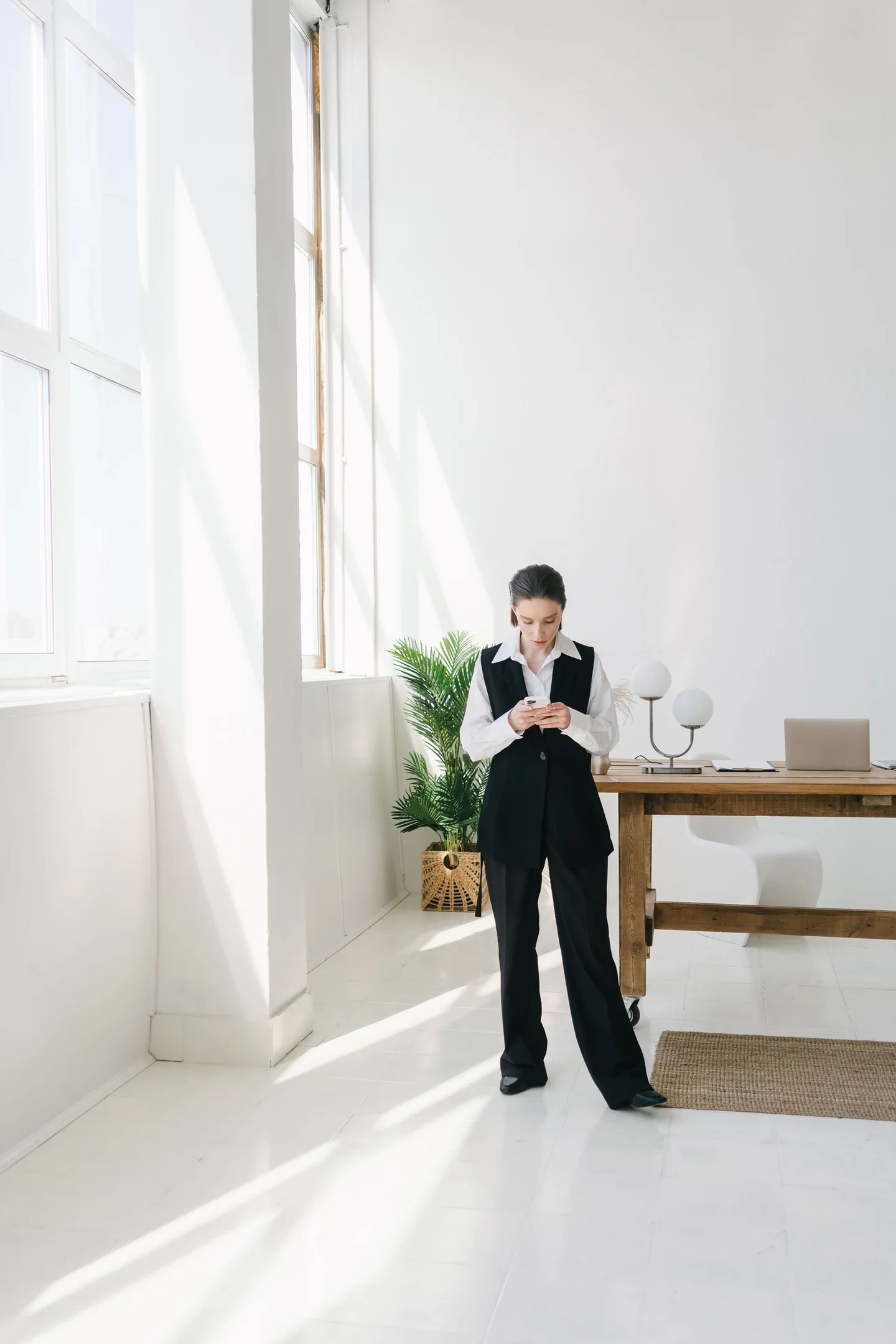 A professional checking her phone in a bright office beside a window